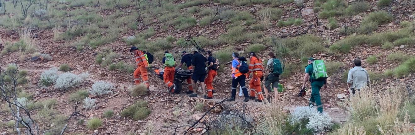 A group of people carrying man on stretcher up a hill.