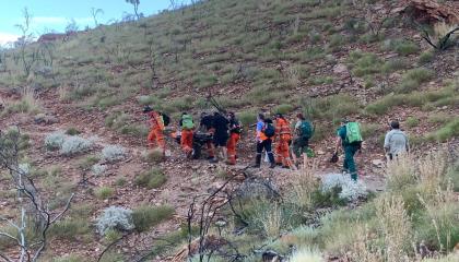 A group of people carrying man on stretcher up a hill.